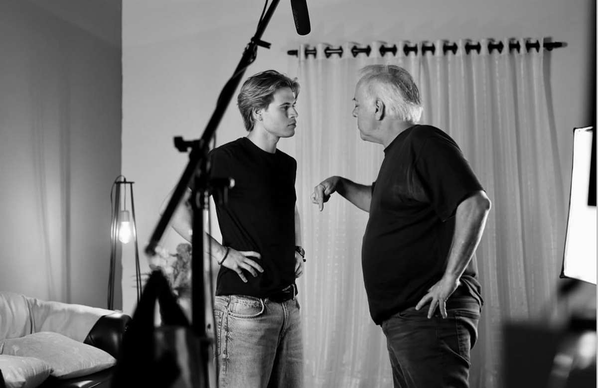 Diretor dando indicação a um ator dentro do set, com microfone boom e refletor no quadro